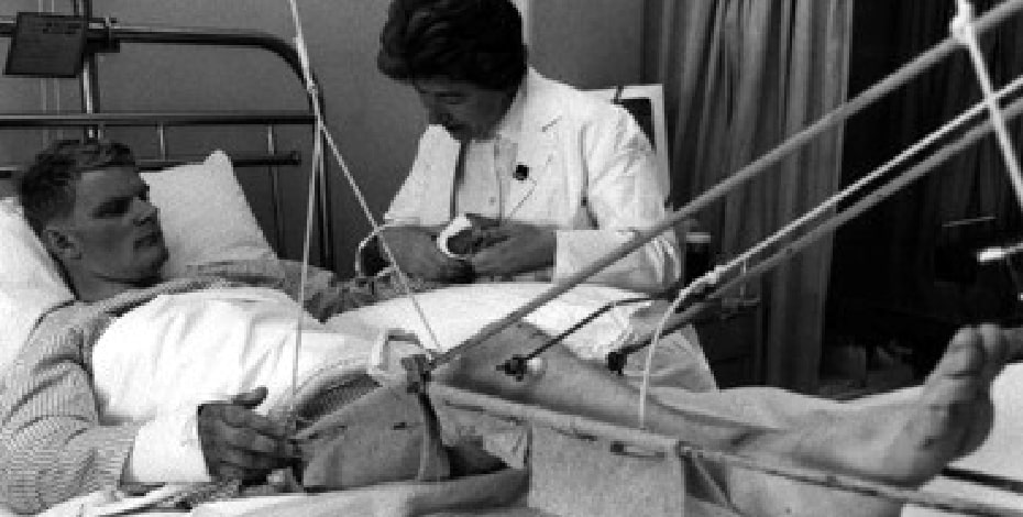 Margaret Nayler treating a patient with multiple injuries. Both arms are in plaster and his right leg is in traction due to a fractured femur.