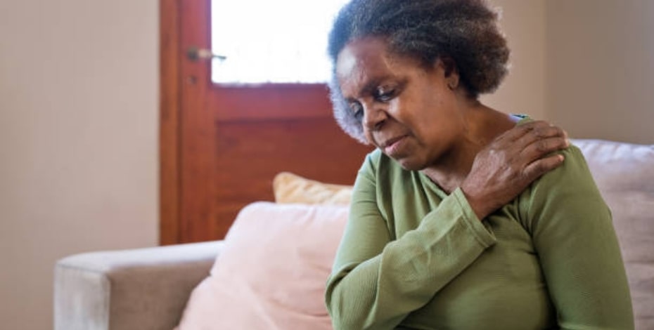 An older woman reaches across and holds her shoulder, like she is slinging an invisible handbag over her shoulder. 