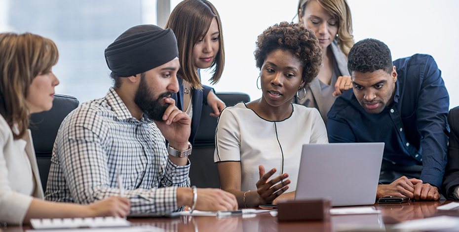 A group of people sitting around an open laptop computer.