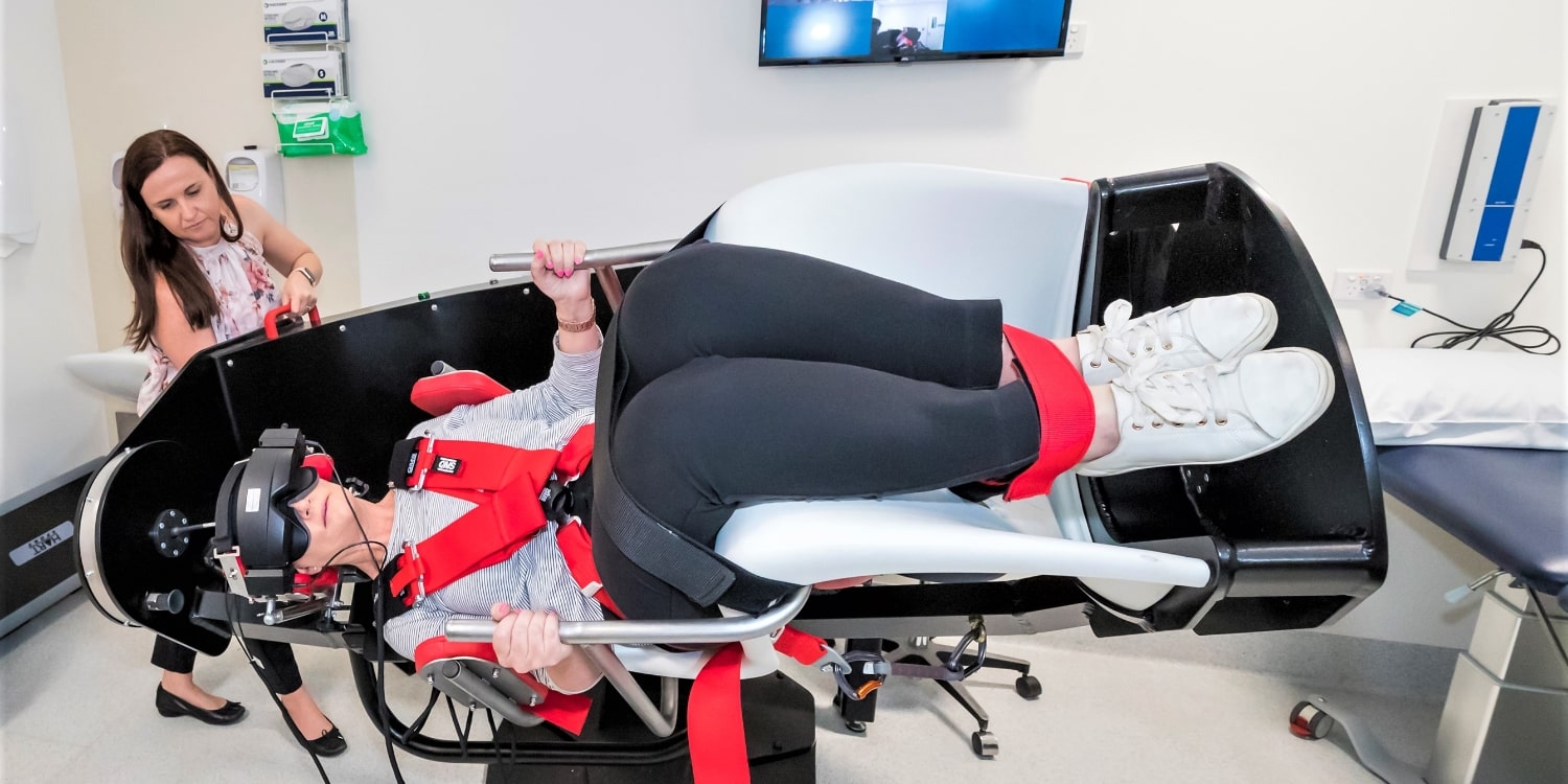 A patient is strapped into a machine that tests their dizziness by rotating them in multi directions.