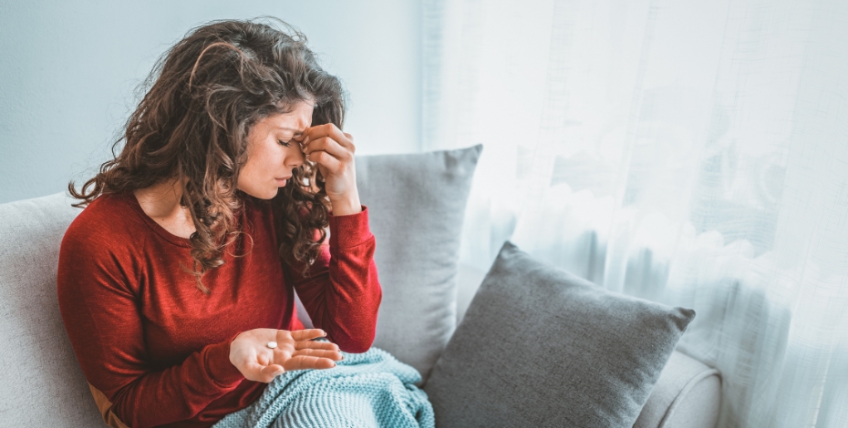 person on a couch holding their head and a tablet in their other hand
