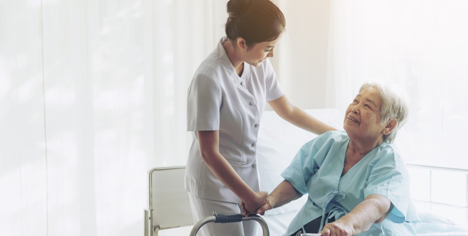 person assisting a patient to stand up from bed with use of a frame