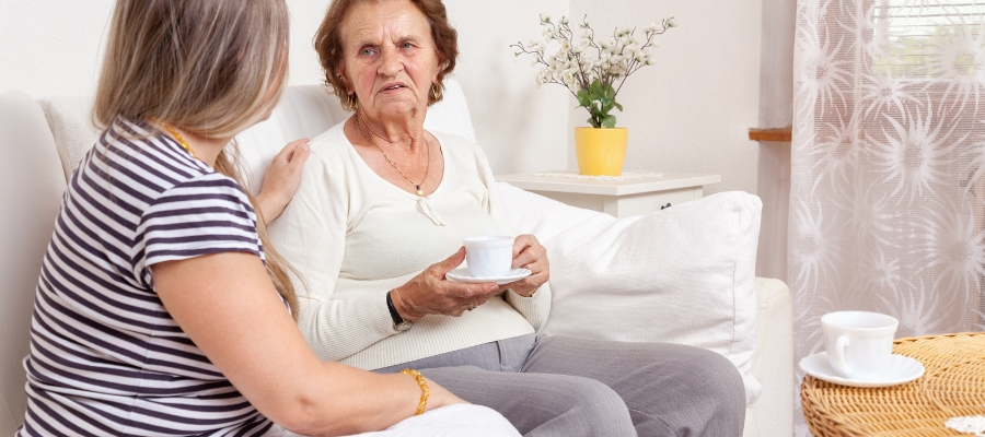 person sitting on a couch holding a tea cup another person with their hand on the shoulder of the first person