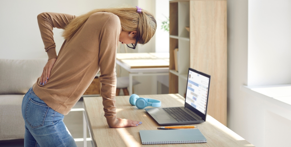 person leaning on a desk holding their back in pain