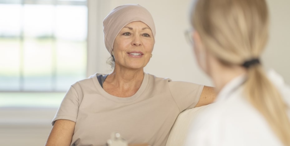 A woman wearing a beige headscarf is talking to another woman with a blonde ponytail. There is a window behind them. 